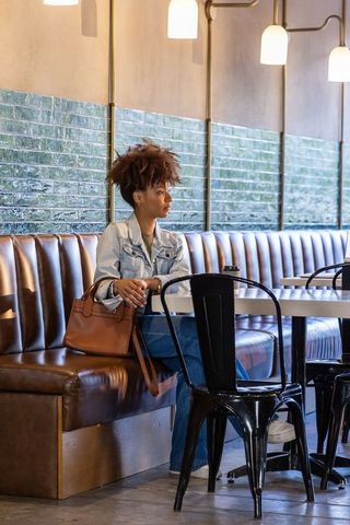 African american woman sitting in stylish cafe booth holding coffee with leather tote