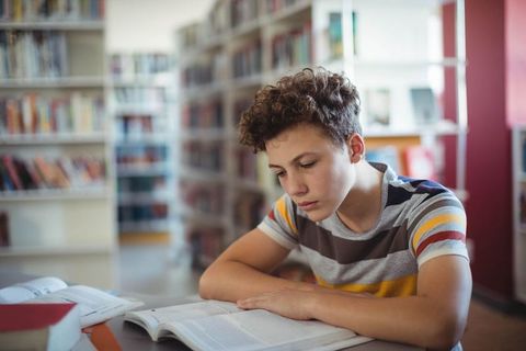 Focused Teen Boy Reading Book in Modern Library Environment