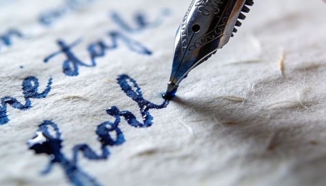 Fountain pen nib writing blue calligraphy handmade paper macro detail ink texture close-up