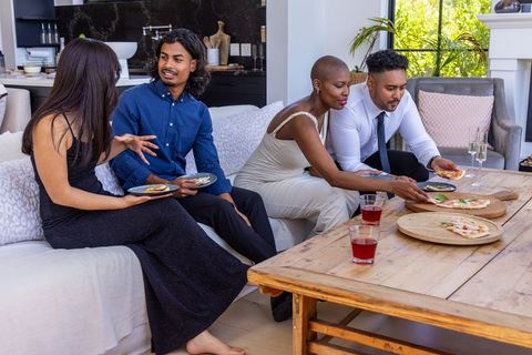 Diverse friends sharing pizza and drinks on rustic table in stylish modern living room