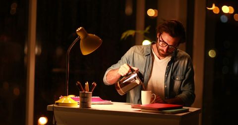 Businessman pouring coffee while working late at office desk