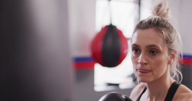 Image of confident, determined caucasian woman in boxing gloves training with punchbag at a gym. Exercise, fitness and healthy lifestyle.