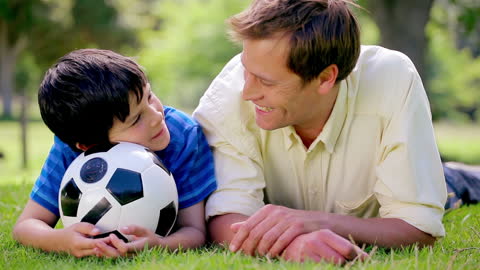Father and Son Relaxing in Grass with Soccer Ball Enjoy Nature