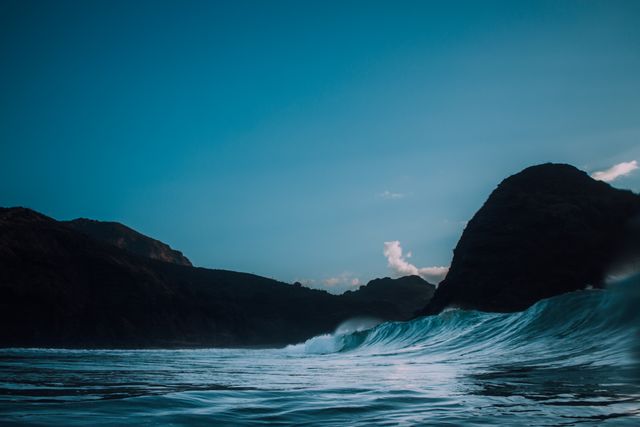 Stunning seascape featuring a majestic wave crashing against a rocky coastline during sunset, with deep blue waters and a serene sky backdrop. Perfect for travel, nature, and outdoor adventure projects.
