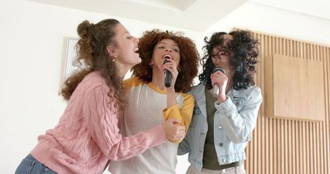 Diverse young women singing with handheld microphones, energetic home karaoke moment