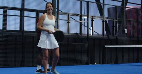 Padel players on an illuminated court smiling widely while preparing for game play. The dynamic environment reflects physical fitness, cooperation, and enjoyment of the sport. Ideal for illustrating active partnerships, team building exercises, modern sports facilities, or marketing sports events and tours.