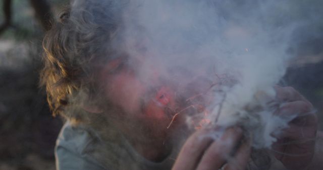 Bearded caucasian male survivalist blowing on smoking tinder to start fire at camp in wilderness - Download Free Stock Photos Pikwizard.com