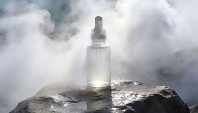 Frosted glass dropper bottle emitting mist on wet rock with condensation and puddles