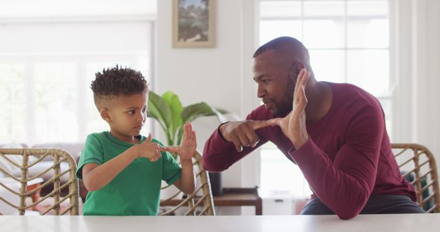 Father teaching young son sign language in a bright living room. Great for content related to family bonding, educational materials, parenting and father-son relationships, learning activities, and communication with special needs.