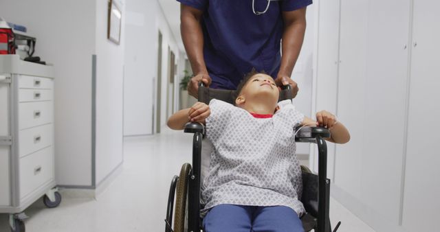 African american male doctor walking with child patient sitting in wheelchair at hospital. Medicine, healthcare, lifestyle and hospital concept.