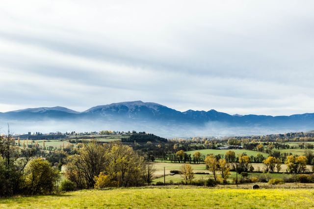 Beautiful panoramic view featuring a serene landscape with rolling hills and farmland against a backdrop of mountains. Ideal for use in travel brochures, nature conservation content, real estate marketing for rural properties, and backgrounds for meditation or relaxation materials.