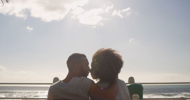 Couple sitting on a bench by the ocean enjoying a romantic sunset, showing affection and togetherness. Useful for themes such as vacation, romance, summer outings, seaside leisure, and romantic getaways.