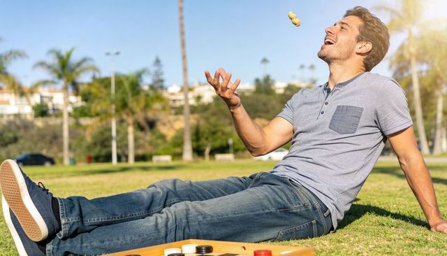 Sunlit park leisure man tossing peanut while lounging on grass with board game pieces