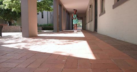 African American teen student walking sunlit campus colonnade with backpack and sneakers