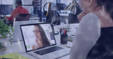 Woman joining virtual meeting at open-plan desk with laptop and coworking collaboration