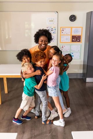 Joyful African American Teacher Embracing Diverse Group of Elementary Students in Bright Classroom