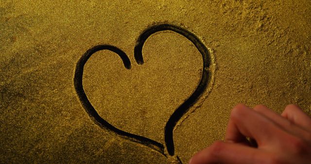 A heart shape is being drawn on a golden glittery surface, with copy space. This simple yet evocative gesture often symbolizes love and affection.