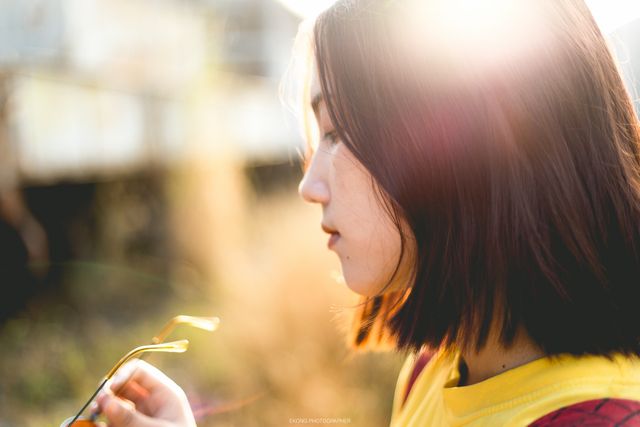 Woman is lost in thought while holding sunglasses in a sunlit outdoor setting. Ideal for concepts like mindfulness, contemplation, relaxation, or beauty in simplicity. Suitable for blogs, mental health articles, wellness campaigns, or outdoor product ads.