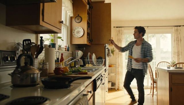 Man reaching into cabinet while preparing meal in sunlit home kitchen with cutting board