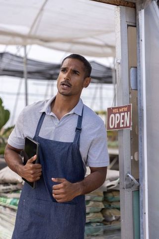 Greenhouse owner greeting customers holding tablet by open sign
