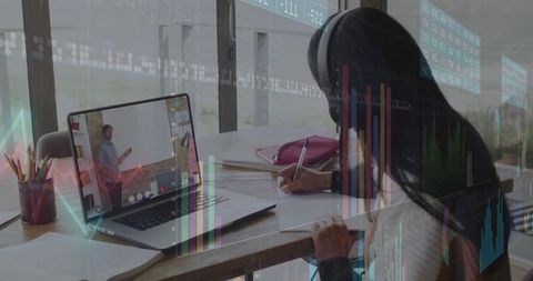 Teen student studying online and writing notes at home desk wearing headset, charts overlay