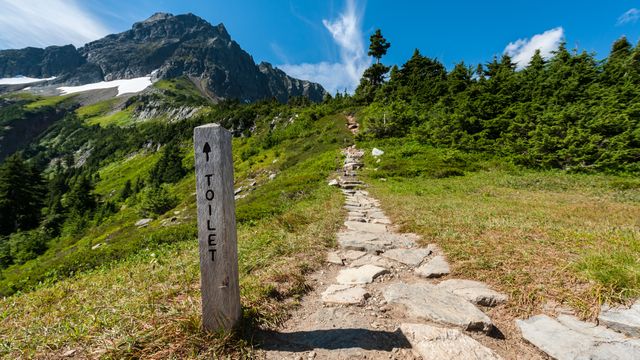 Pathway in mountainous landscape leading to an outdoor toilet; useful for content about outdoor activities, hiking tips, exploration, and nature destinations. Ideal for nature blogs, travel brochures, adventure websites.