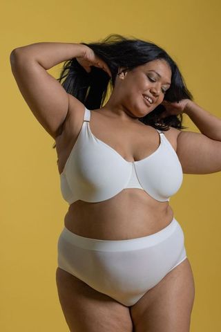 Curvy woman wearing white underwire bra and high-waist briefs smiling on yellow backdrop