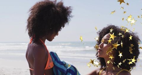 Mother and daughter holding towel on sunny beach with floating gold star confetti