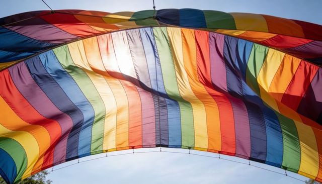Billowing rainbow canopy filtering sunlight over open sky parachute fabric arch with cords
