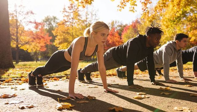 Autumn outdoor group performing push-ups on park pathway for fall fitness training