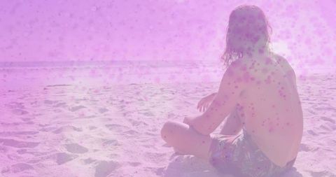 Backlit man sitting on sandy beach watching pink sun glare over ocean horizon