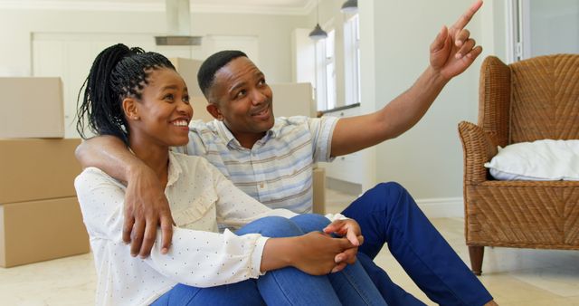 Front view of happy young black couple sitting on floor and interacting with each other at home. Man pointing up by finger 4k
