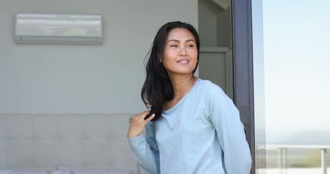 Calm asian woman enjoying morning light in minimalist bedroom with balcony view