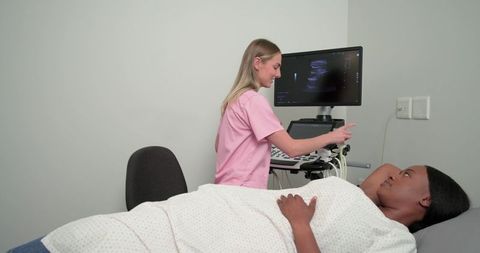 Sonographer pointing at ultrasound monitor during abdominal scan while patient lying on bed