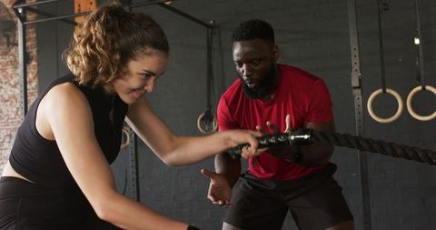 Gym trainer coaching woman with battle rope exercise challenge