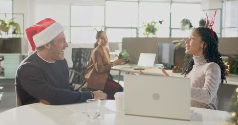 Diverse coworkers celebrating holiday at office table wearing Santa hat and antlers