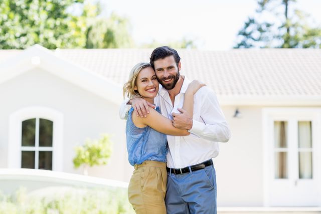 Happy couple embracing outside their new home, smiling and enjoying the moment. Perfect for real estate promotions, homeownership advertisements, family lifestyle blogs, and relationship articles.