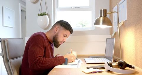 Focused man writing in home office with laptop and coffee