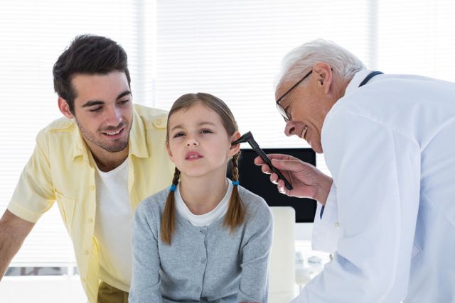 Doctor examining young girl's ear with an otoscope while her father watches. Ideal for use in healthcare, medical, pediatric, and family-related content. Can be used in articles, brochures, and websites focusing on child health, medical checkups, and family care.