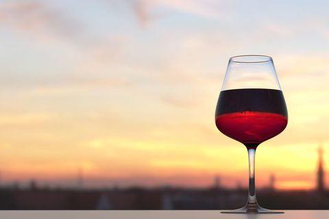 Red Wine Glass Capturing Golden Sunset Over Blurred City Skyline for Romantic Evenings