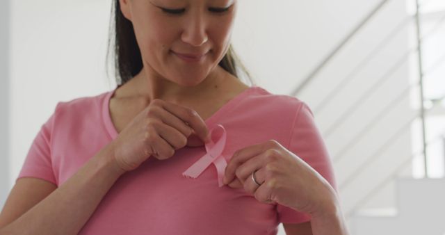 Happy asian woman in pink tshirt showing pink ribbon at home - Download Free Stock Photos Pikwizard.com