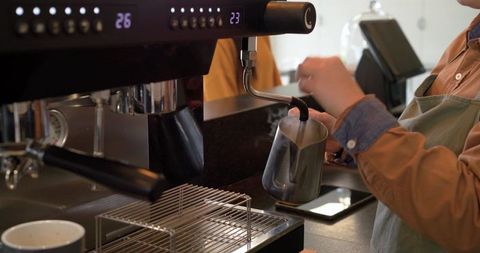 Barista steaming milk with stainless pitcher at espresso machine for latte art