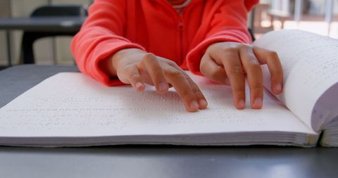 Blind boy reading braille book in school classroom setting