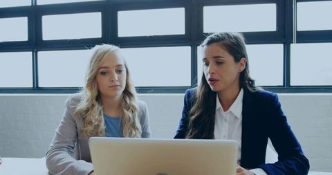 Female colleagues collaborating over laptop in bright modern office meeting