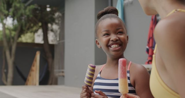 Smiling girl and friend enjoying colorful popsicles. Ideal for stock images for summer, outdoor activities, childhood, friendship, and happiness themes. Could be used for promoting family-friendly products, summer snacks, or vacation activities.