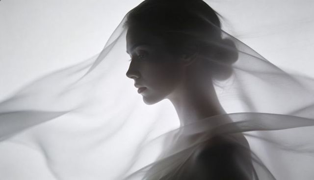 Ethereal backlit profile of woman wearing translucent veil with flowing fabric motion