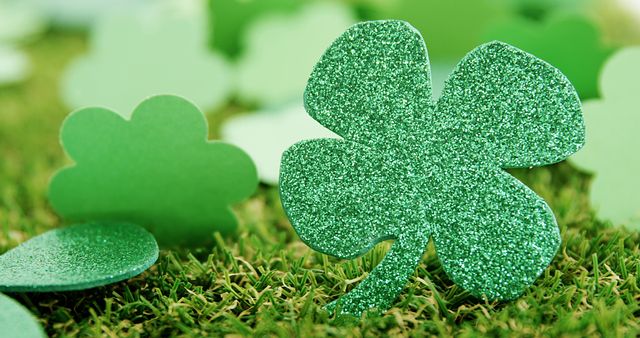 A glittering green shamrock stands out among other clover cutouts on a grassy surface, symbolizing luck and the celebration of St. Patrick's Day. Its sparkling texture adds a festive touch to the traditional Irish symbol.