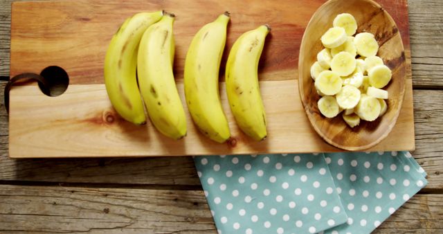 A bunch of bananas lies next to sliced banana pieces on a wooden cutting board, with copy space. This setup is perfect for culinary themes, emphasizing healthy eating and food preparation.
