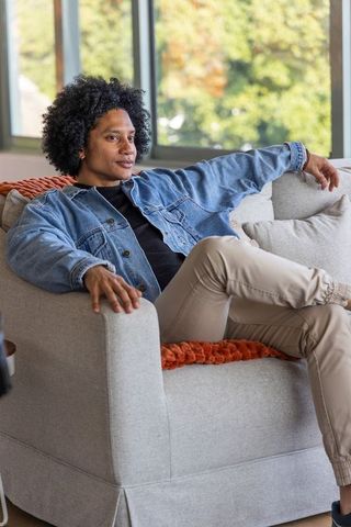 African american man relaxing on sofa by window wearing denim jacket and beige pants