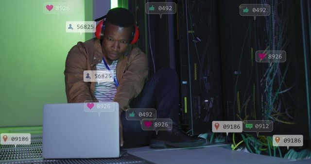 Image of social media icons over african american male engineer using laptop at server room. Social media networking and business data storage technology concept